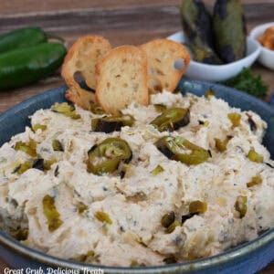 A blue bowl filled with roasted jalapeno artichoke dip with three crusty pieces on bread stuck in the dip
