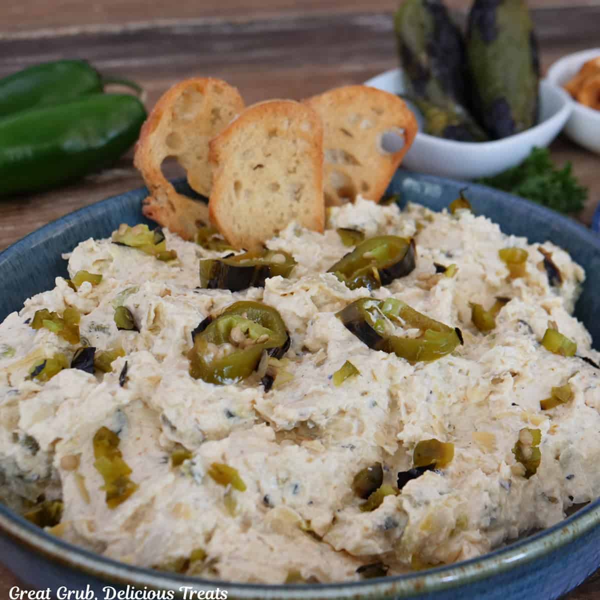 A blue bowl filled with roasted jalapeno artichoke dip with three crusty pieces on bread stuck in the dip