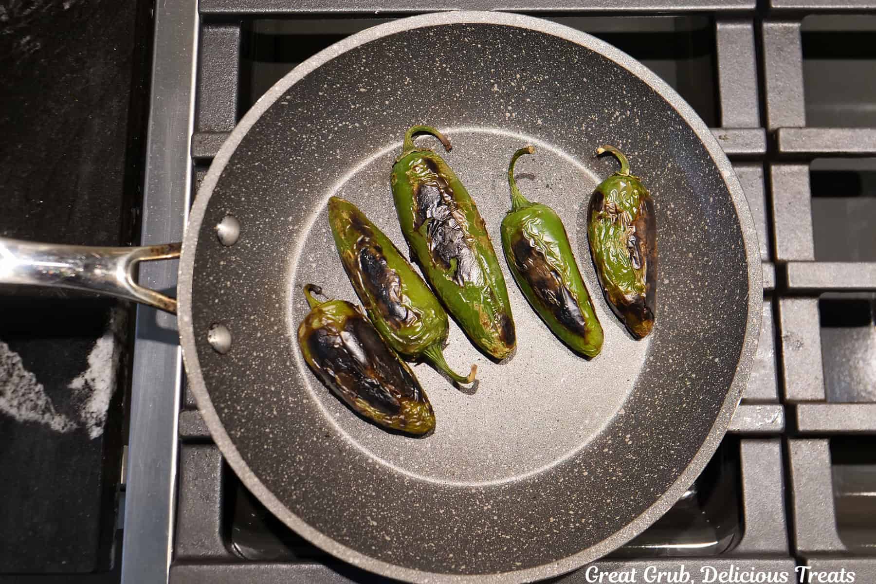 A frying pan with five roasted jalapenos in it.