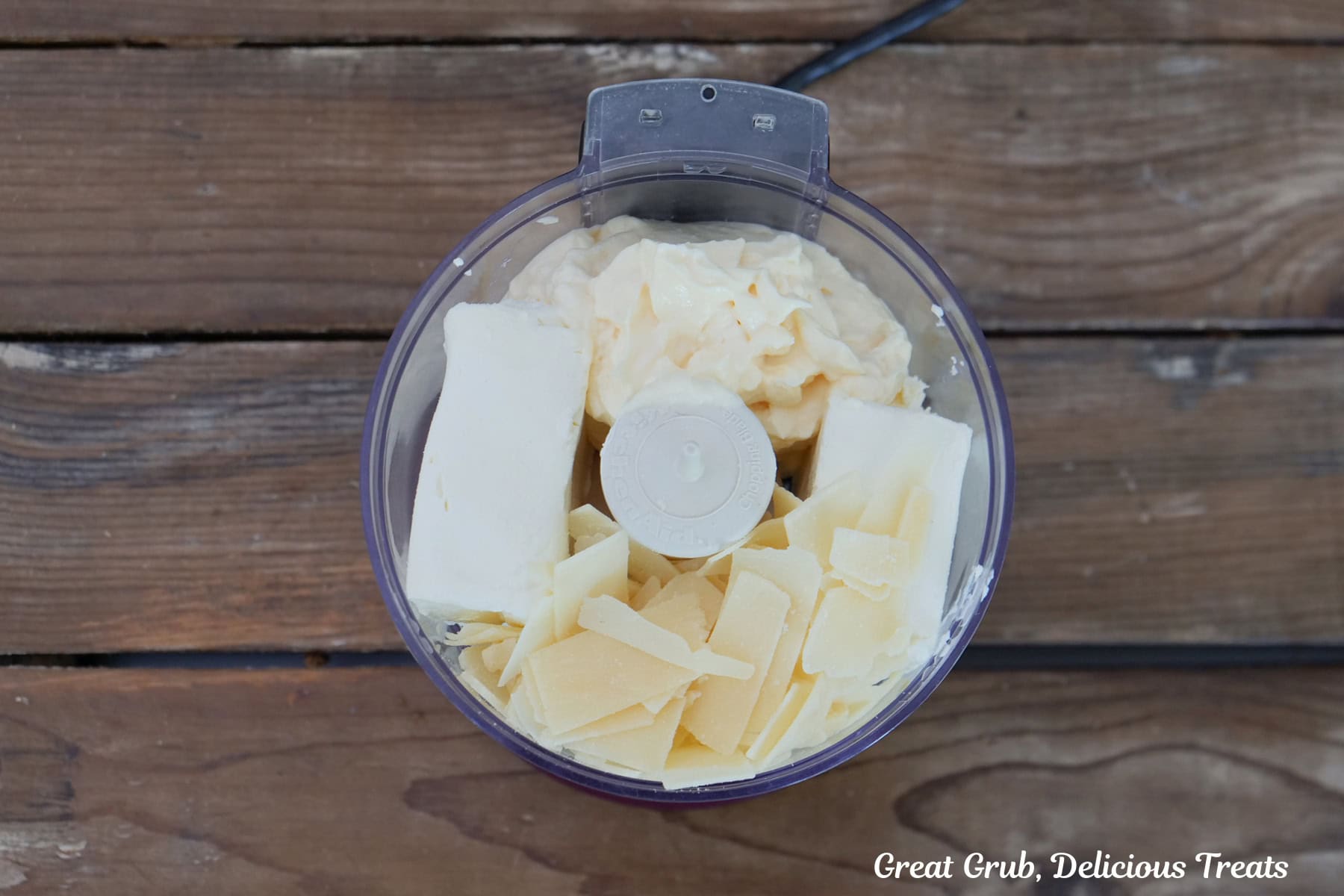 A small food processor with mayonnaise, shaved Parmesan, and cream cheese in it before being mixed together.