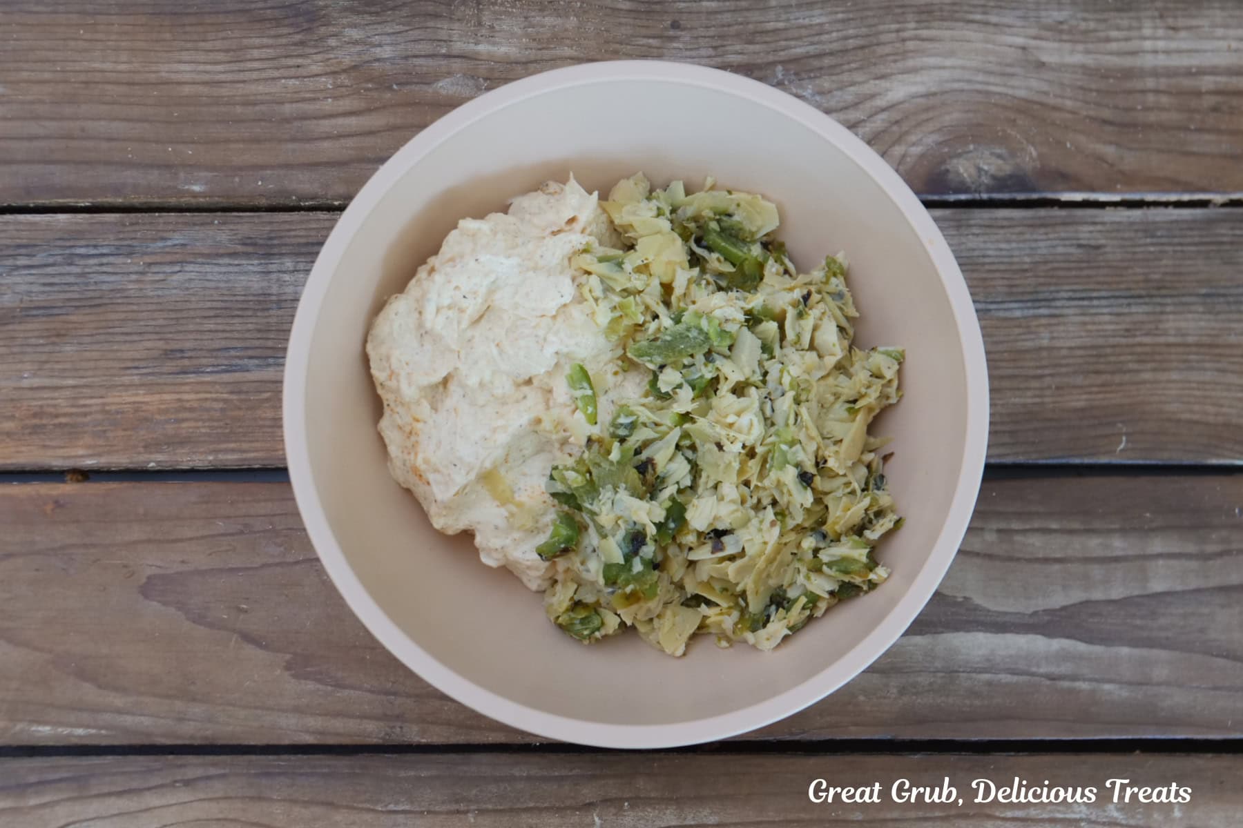 A white bowl with the cheesy mixture and the jalapeno artichoke mixture in it before being stirred and combined.
