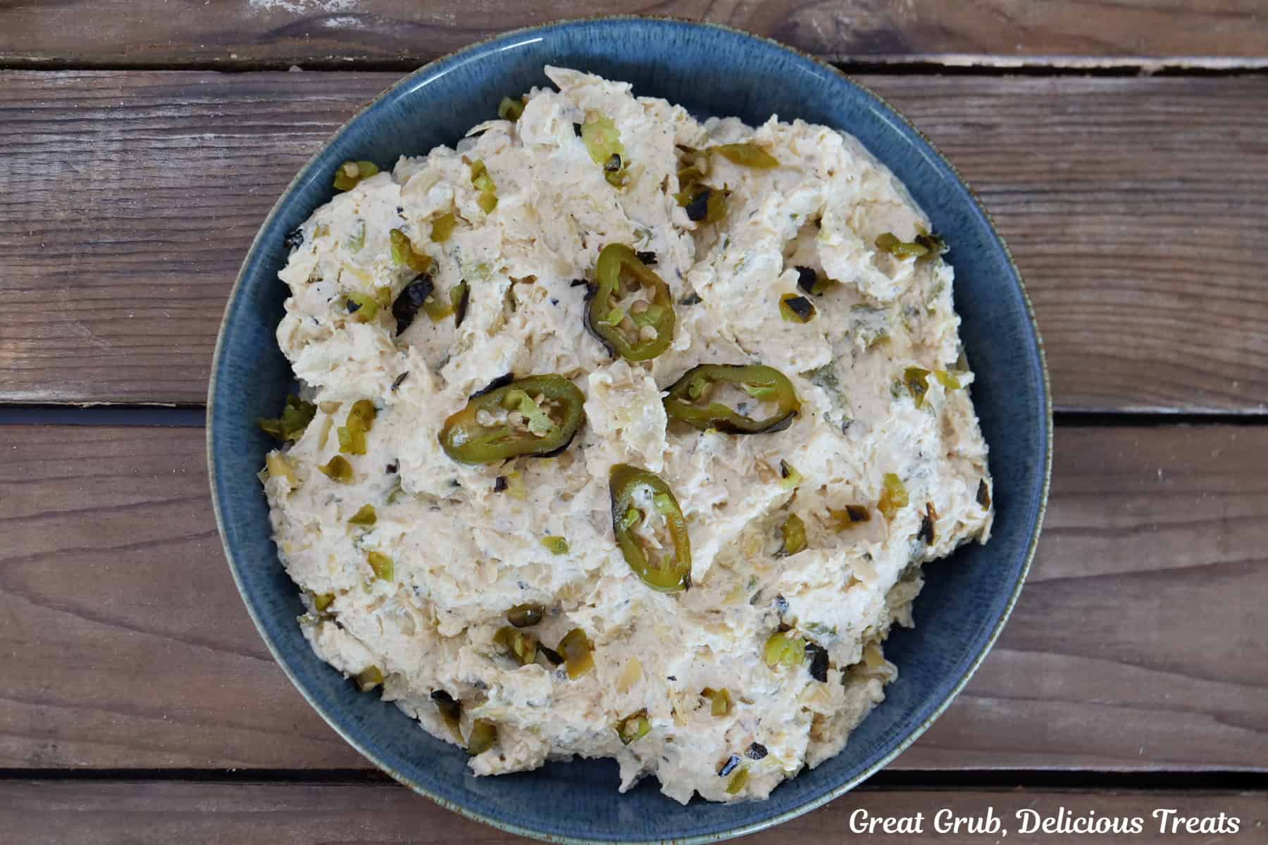 A rustic wood surface with roasted jalapeno artichoke dip in it topped with a few slices of roasted jalapenos.